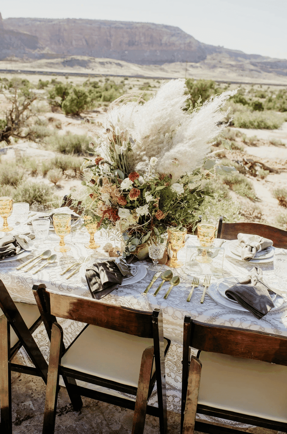Elegant outdoor table setting with floral centerpiece in a desert landscape.