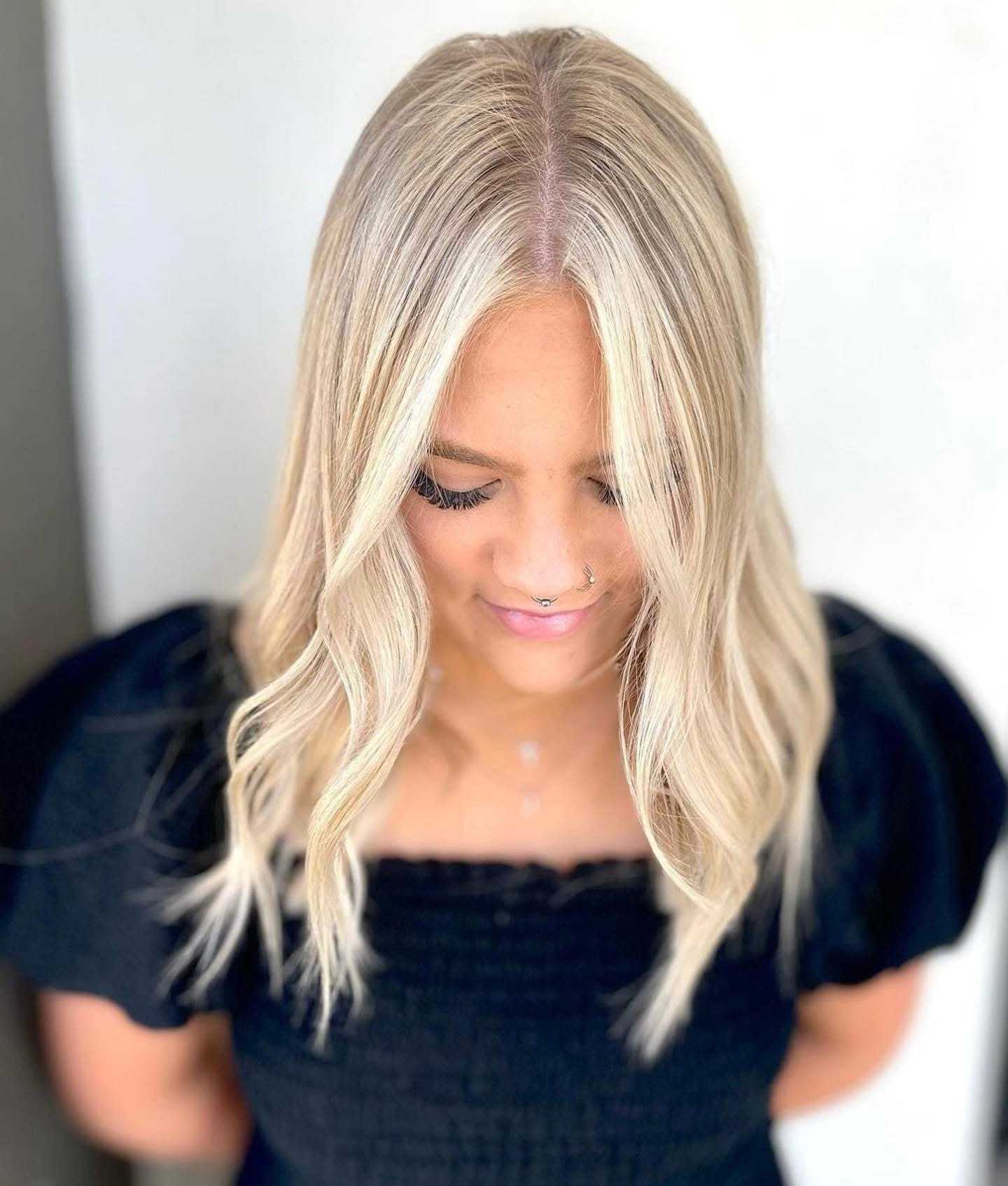 Woman with wavy blonde hair in a black top, looking down, displaying elegant hairstyle.